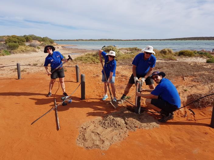 Four people work to erect a fence on a beach front